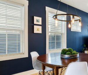 Modern dining room with dark blue walls, oval table, pendant lights, and framed artwork.